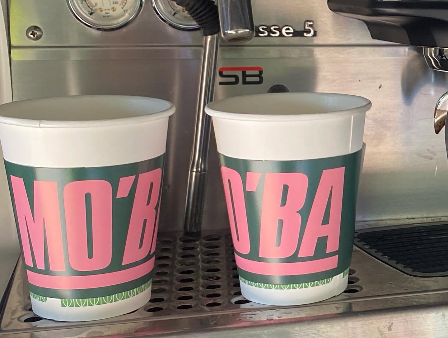 Two MO'BA cups resting on the drip tray of the espresso machine inside the mobile bar.