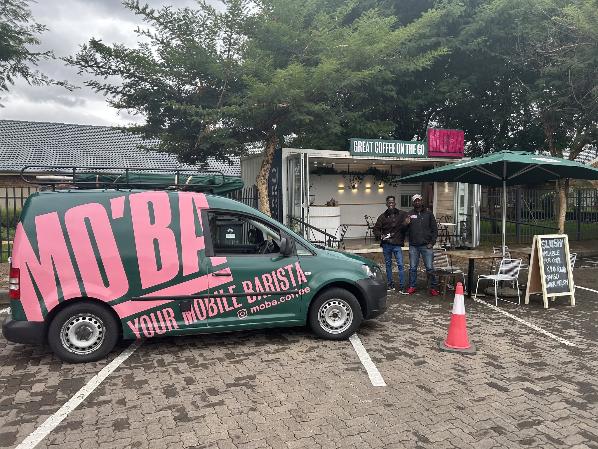 The MO'BA van parked outside a branded container coffee bar, with two staff members ready to serve.