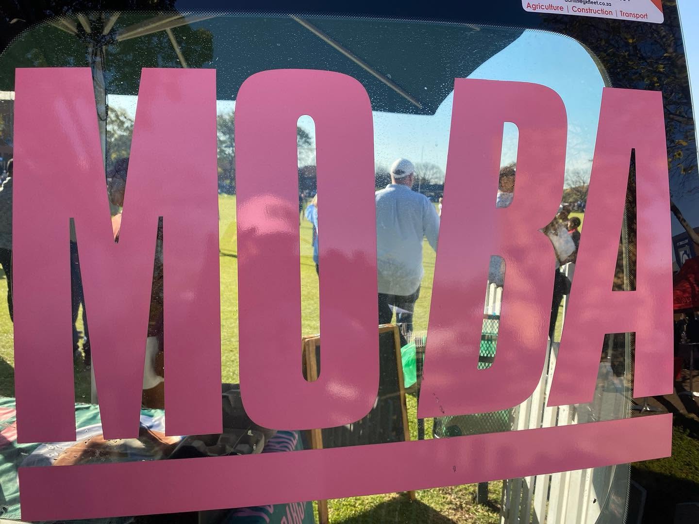 The MO'BA logo on the van window, reflecting a school sports field in the background.